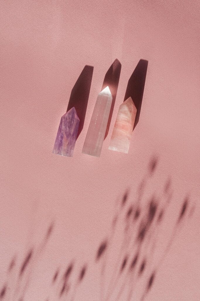 Three polished crystals casting shadows on a soft pink surface, creating a tranquil and mystical feel.